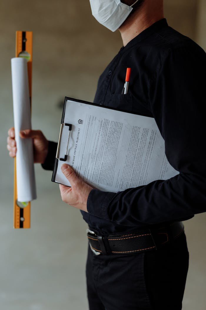 Architect wearing a face mask holds blueprints and clipboard, emphasizing safety measures.